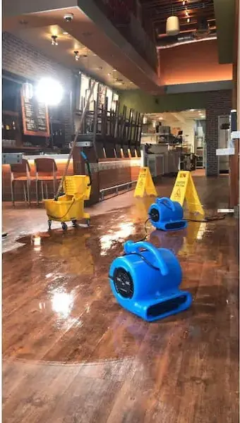 Air movers drying a wet hardwood floor in a restaurant dining room