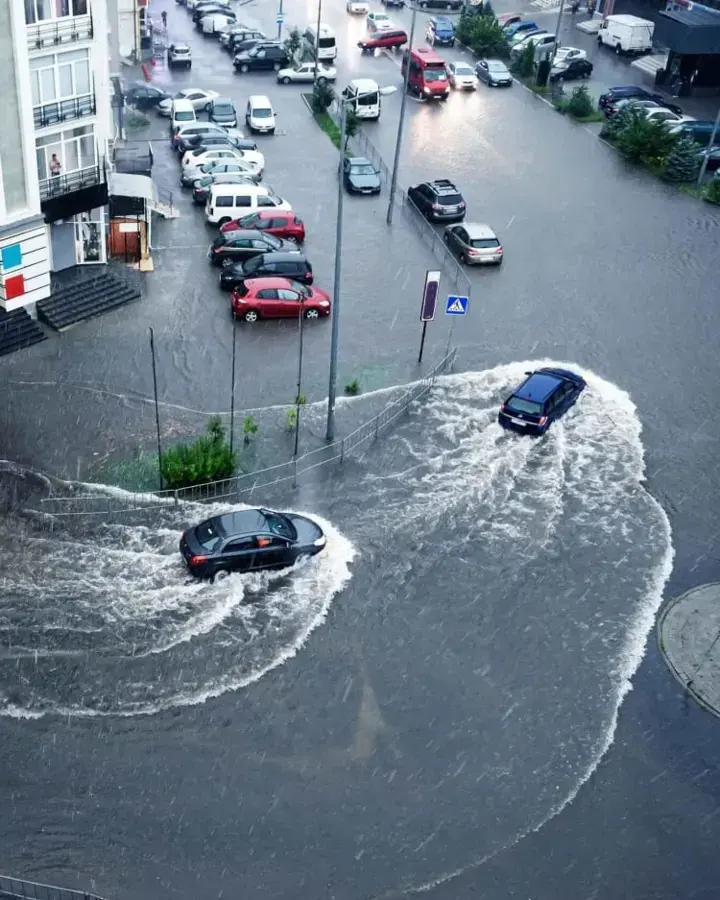 Floodwater covering a street with cars driving through it